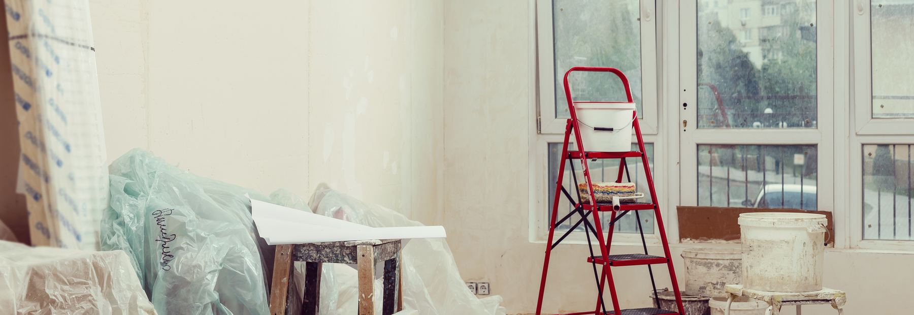 Interior painting in progress with ladder, roller tray and protected floors